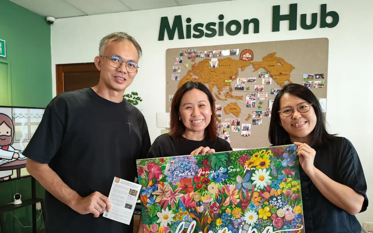Pastor Jony with two friends at the Mission Hub, holding a flower painting